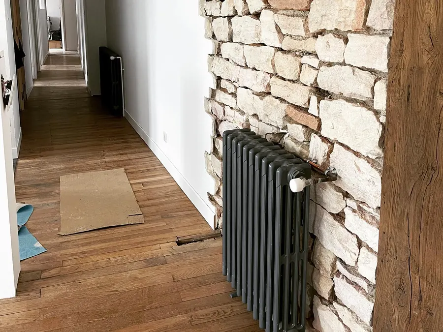 Radiateur en fonte installé contre un mur de pierre lors d’une rénovation à Lugny